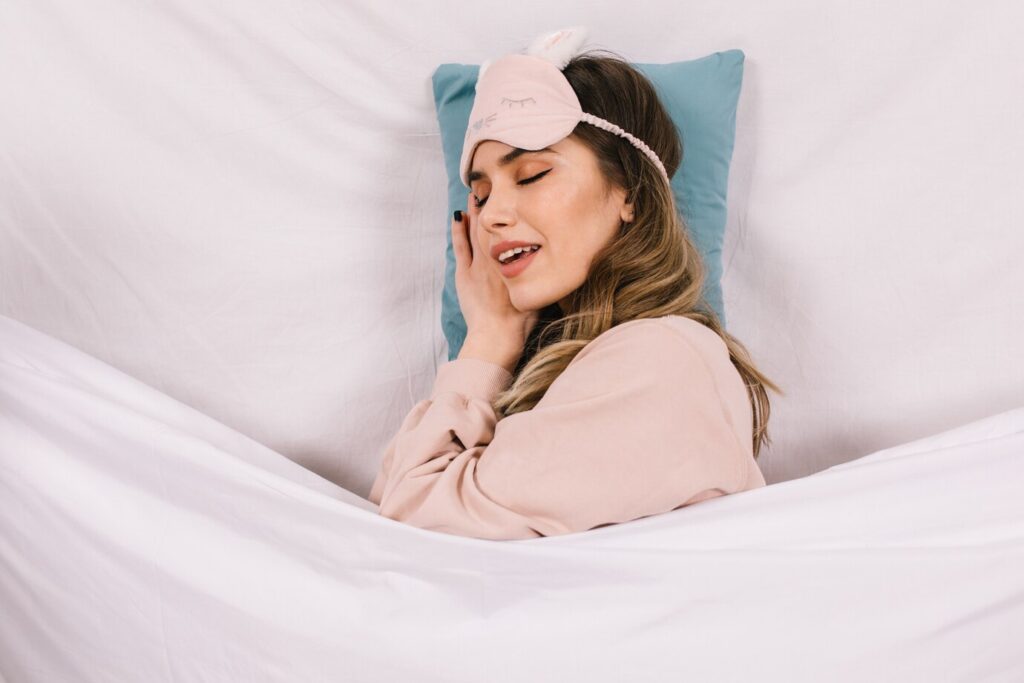 person lies cozy in bed, wearing a soft sleep mask