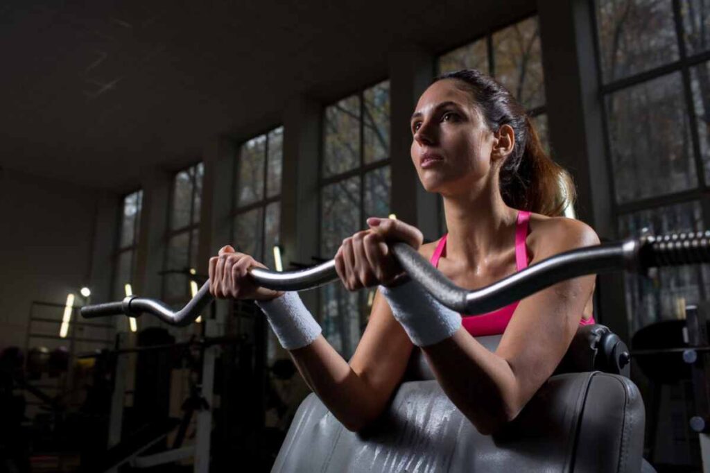 person wearing a pink tank top and wristbands is gripping a barbell