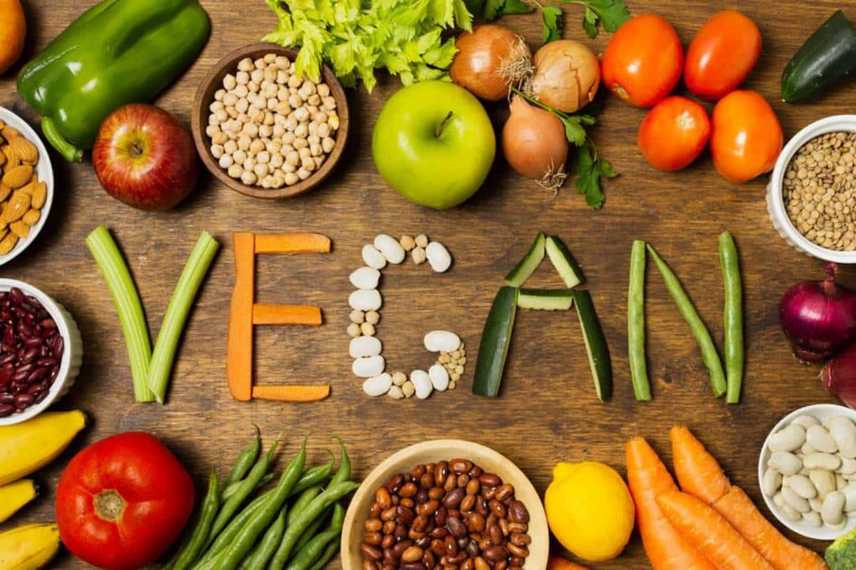 A colorful array of vegetables, beans, and nuts arranged to spell "VEGAN" on a wooden table, promoting a plant-based lifestyle.